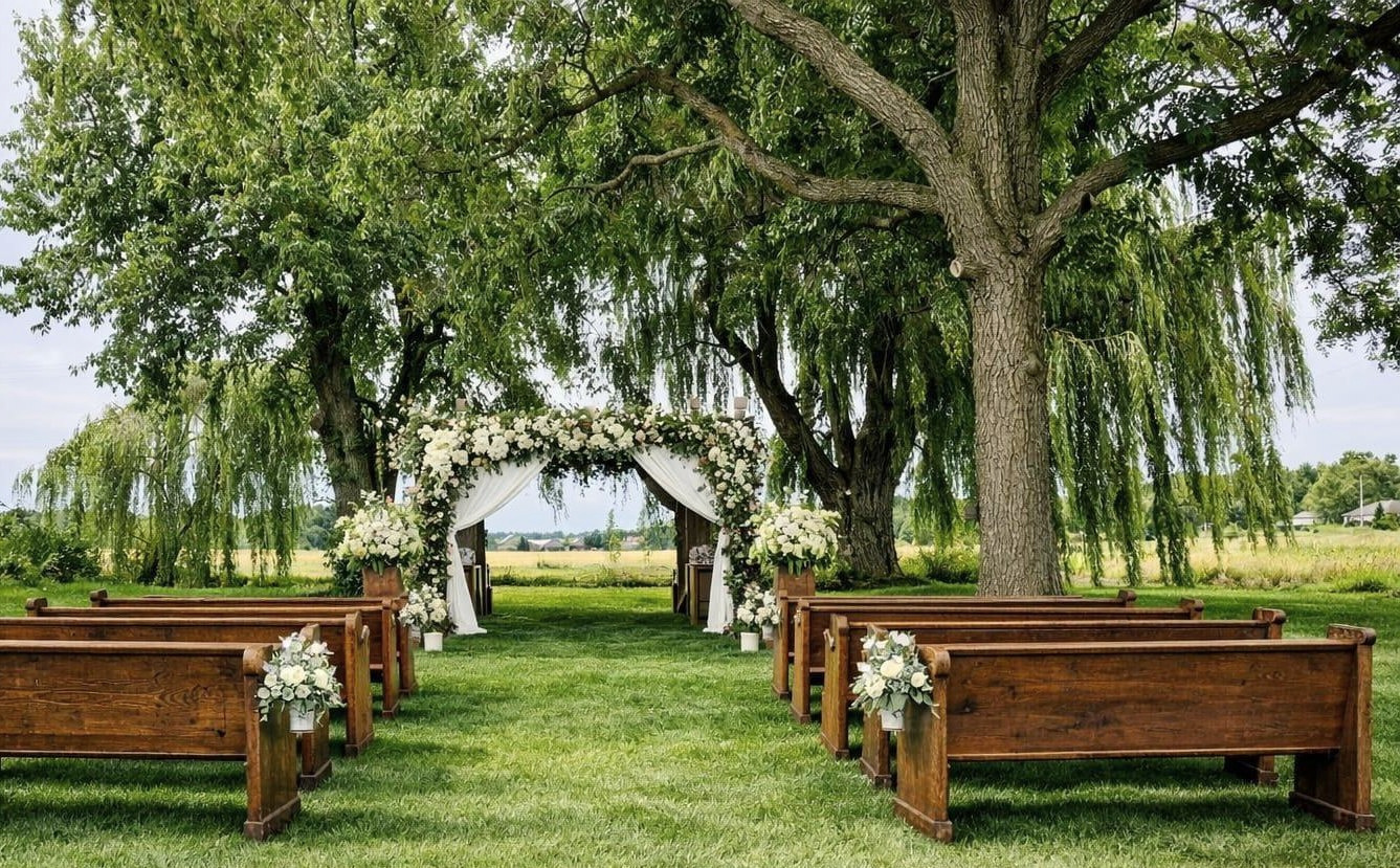 Ceremony setup with wooden church pews and floral arch beneath the willows