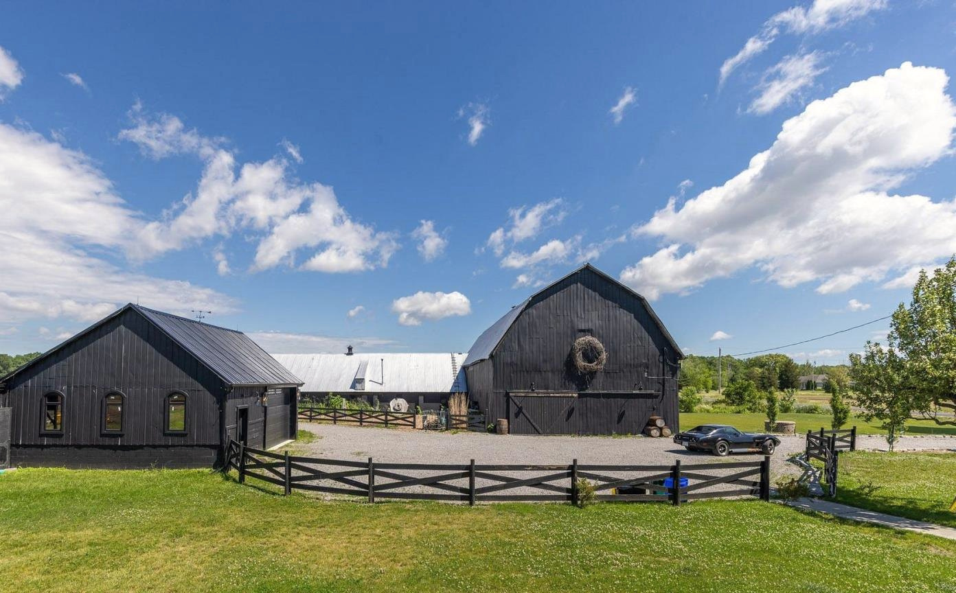 The black barn and outbuildings behind wooden fencing under a summer sky
