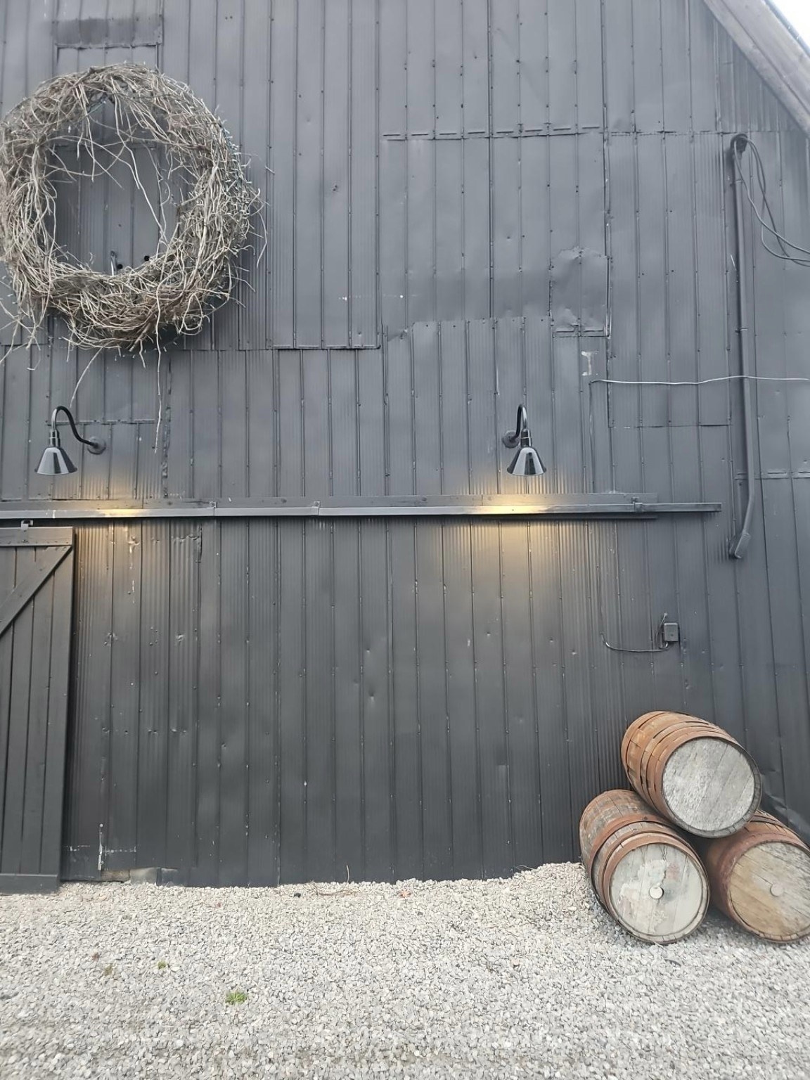 Black barn siding with wreath, lights and wine barrels